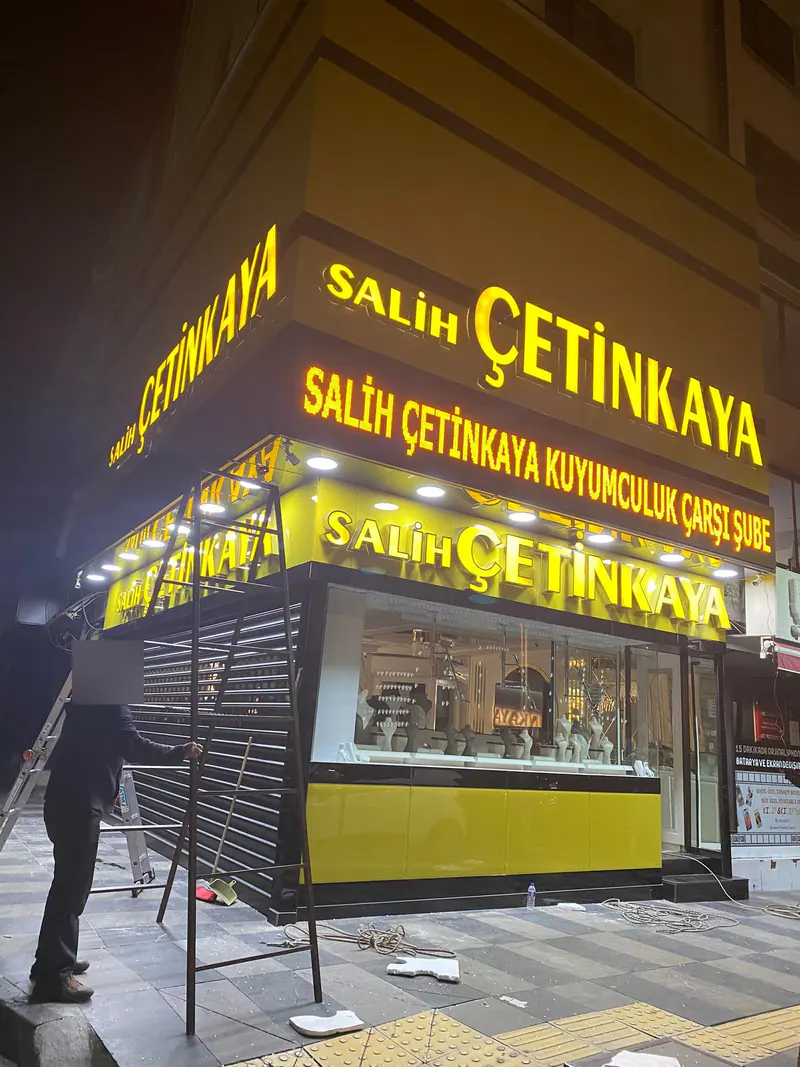 Gece yapılan tabela montajı; merdiven üzerinde çalışan usta ve yanan sarı kutu harfler