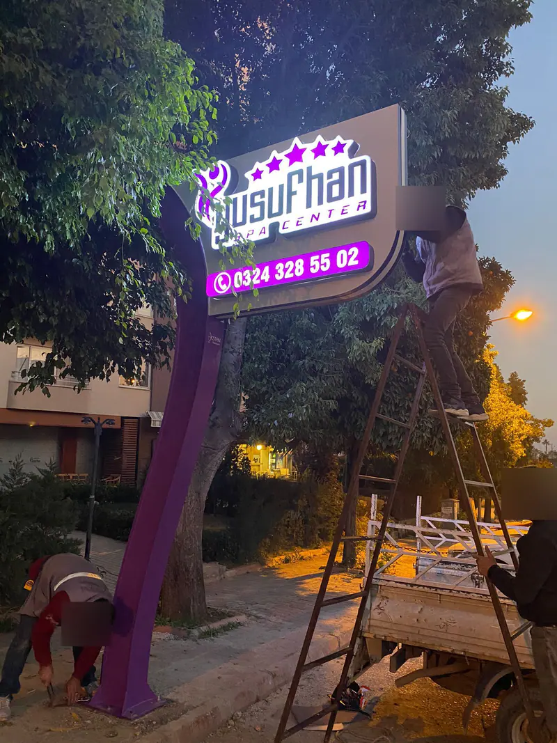 Alacakaranlıkta totem tabelanın yerine kaldırılması; merdiven, kamyonet ve montaj ekibi